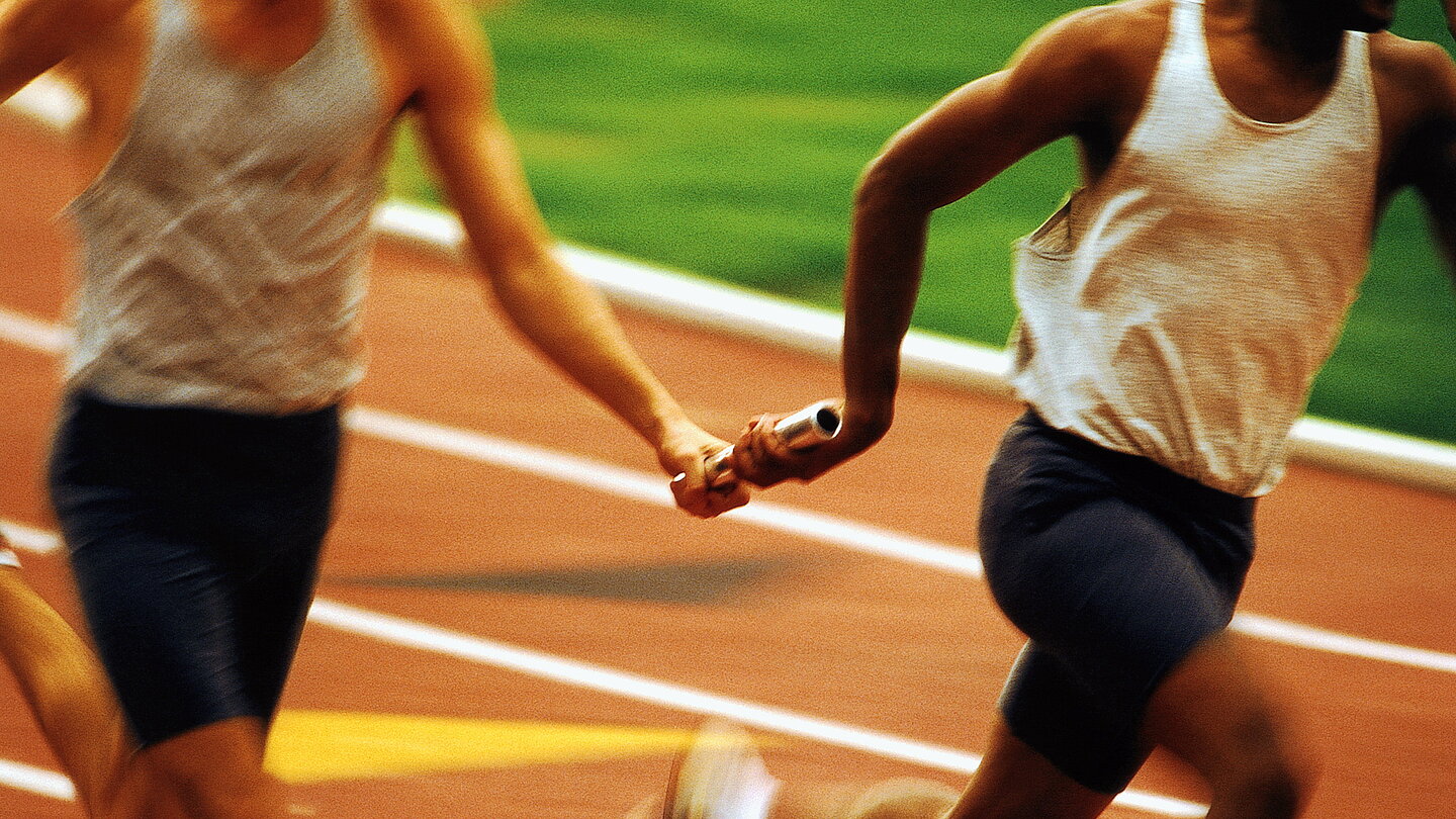 Relay racers passing baton, mid section (blurred motion)